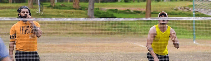 Two men playing badminton, a net with trees behind near Avana Resort