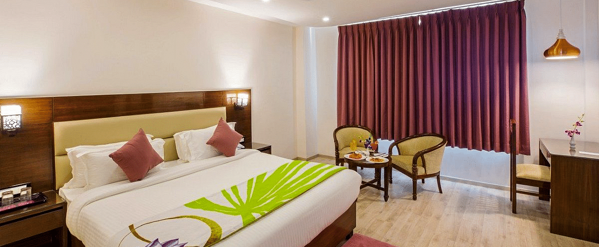 A wide angle shot of the Premium Room with a red carpet in front of the double bed along with a work station in the corner of Regenta Inn DLS.