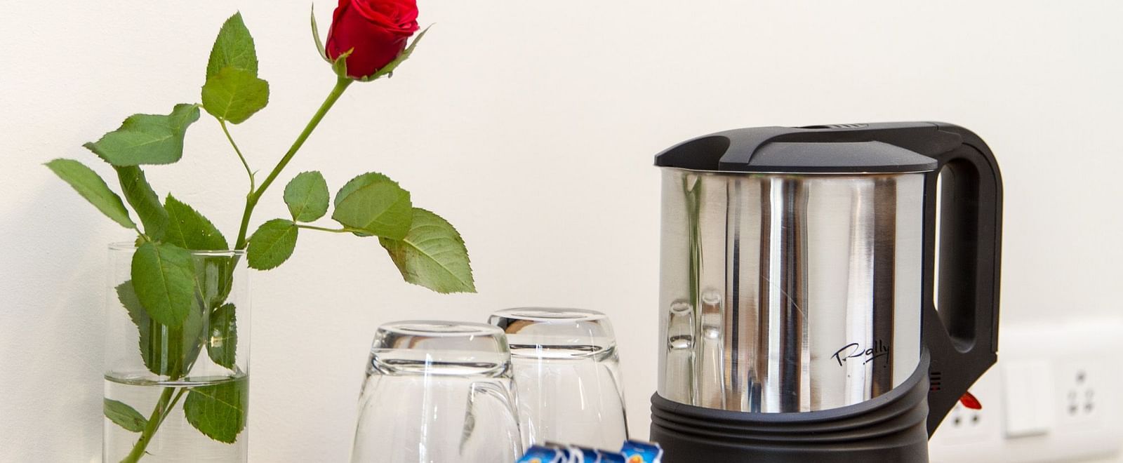 A kettle and glasses placed on a tray and a small vase with a single red rose beside it - Sanctum Suites Whitefield, Bangalore