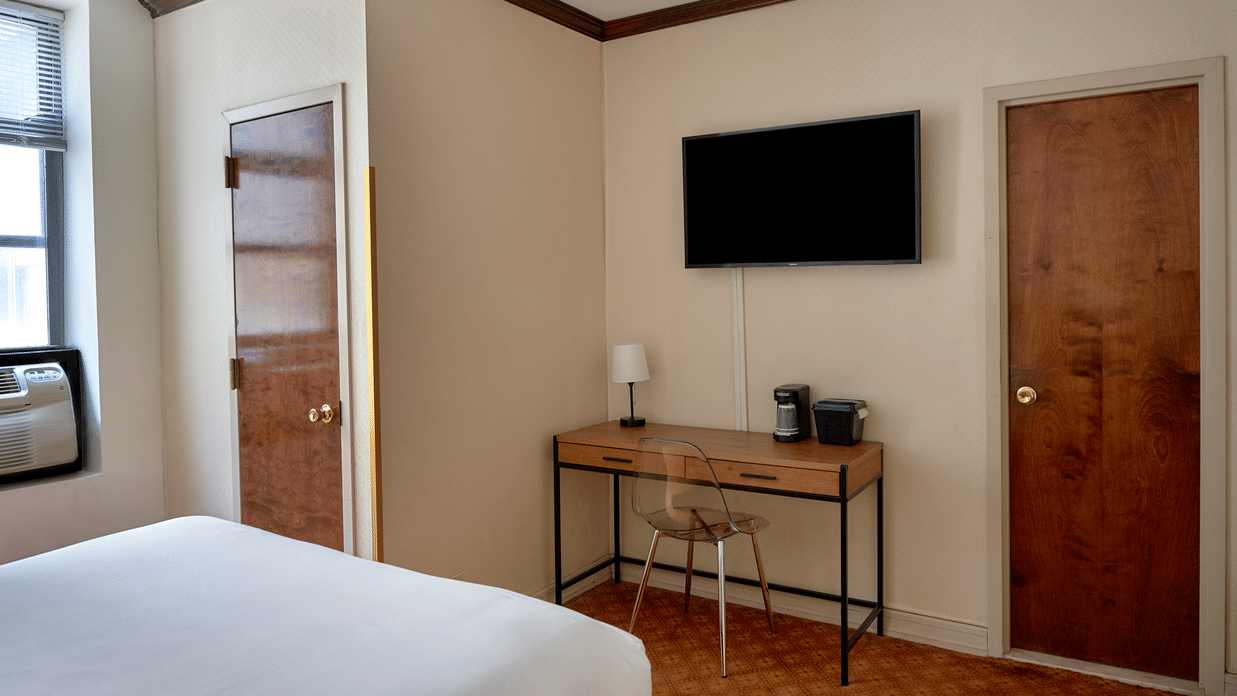 Guest room at Night Hotel Broadway with a mounted TV, desk, chair, and bed in view.