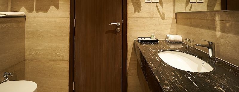 A bathroom with a sink, mirror, wooden door, and towel rack at The Hamuse Hotel, Kodaikanal.