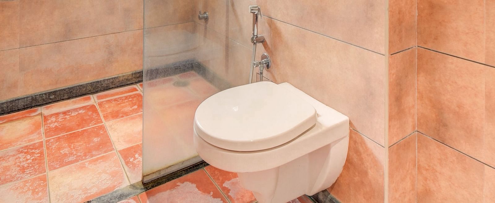 A spacious washroom at Harigovinda's JNStay with a western toilet and a glass panel separating the shower area