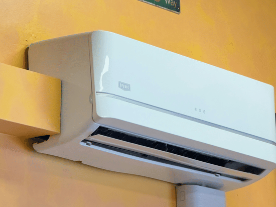 A wall-mounted split air-conditioner with a yellow-coloured wall behind it.