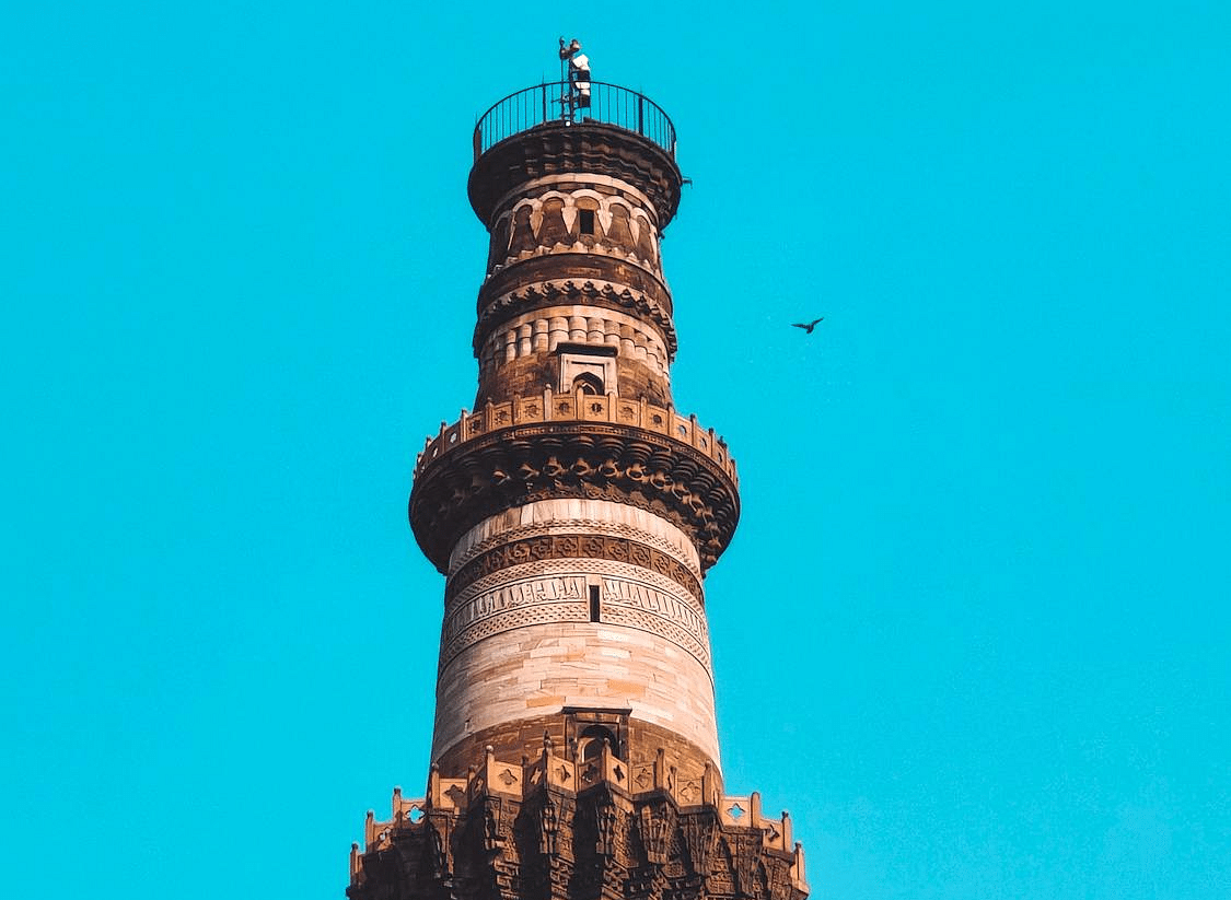 An image of the Qutub Minar against a clear sky, with a bird soaring in the background.