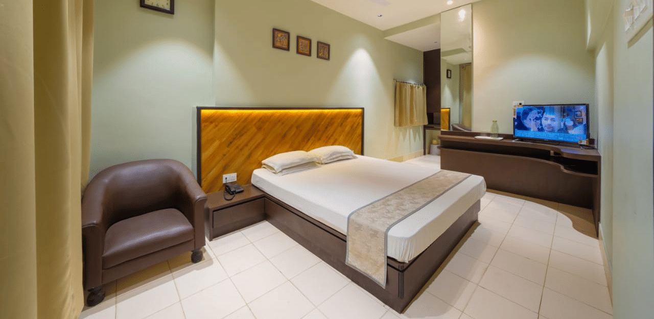 Minimalist bedroom featuring a double bed, wooden headboard, a seating area, and a TV on a wooden cabinet – Hotel Dolphin Puri
