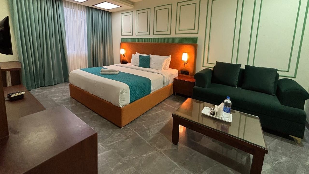 A spacious room with a double bed, a dark green sofa, and a wooden coffee table - Asian Suites IFFCO Metro, Gurgaon