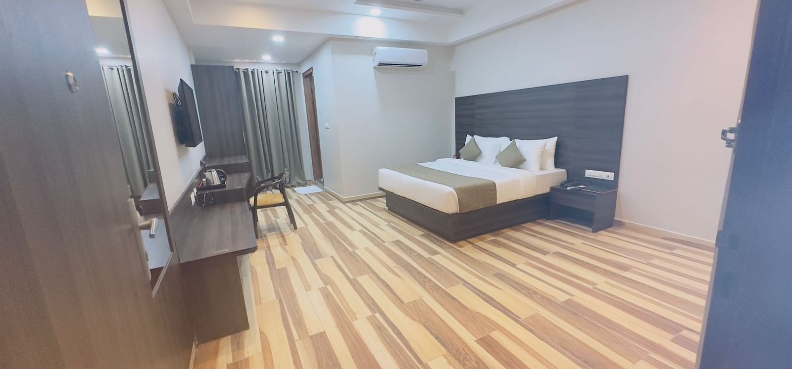 A slightly wider view of a room with a double bed, dark furniture, and wooden flooring - Kankidham Lords Inn