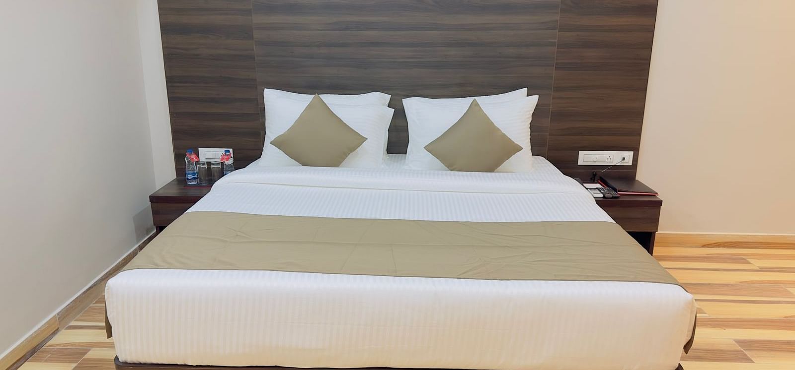 A close-up of a double bed with beige and white linens and a dark headboard - Kankidham Lords Inn