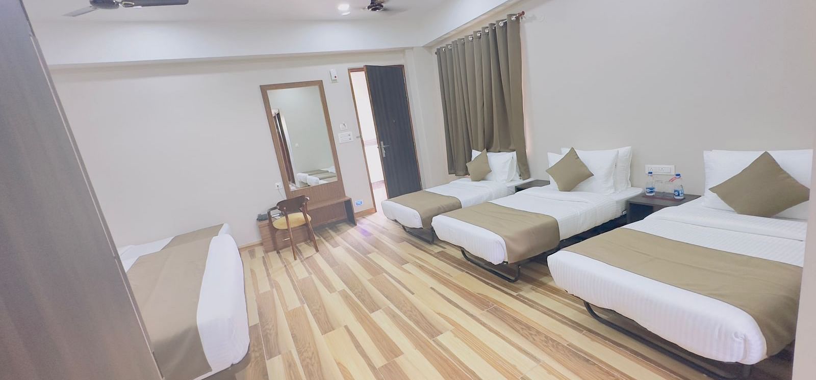 A spacious room features double beds with white and beige bedding, wooden floors, and ceiling fans - Kankidham Lords Inn