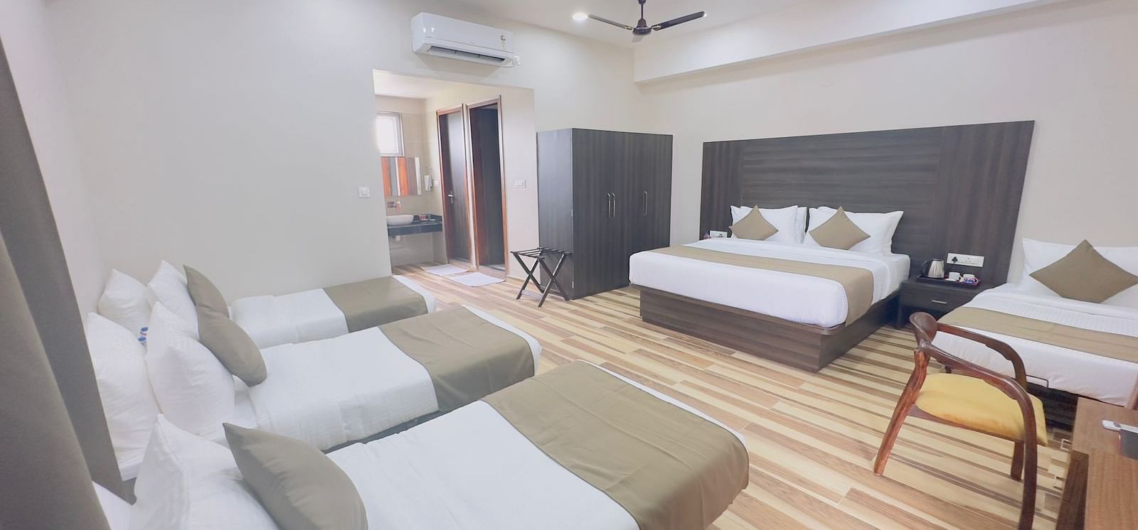 A hotel room contains double beds with white bedding, a single bed, a table, and wooden flooring - Kankidham Lords Inn