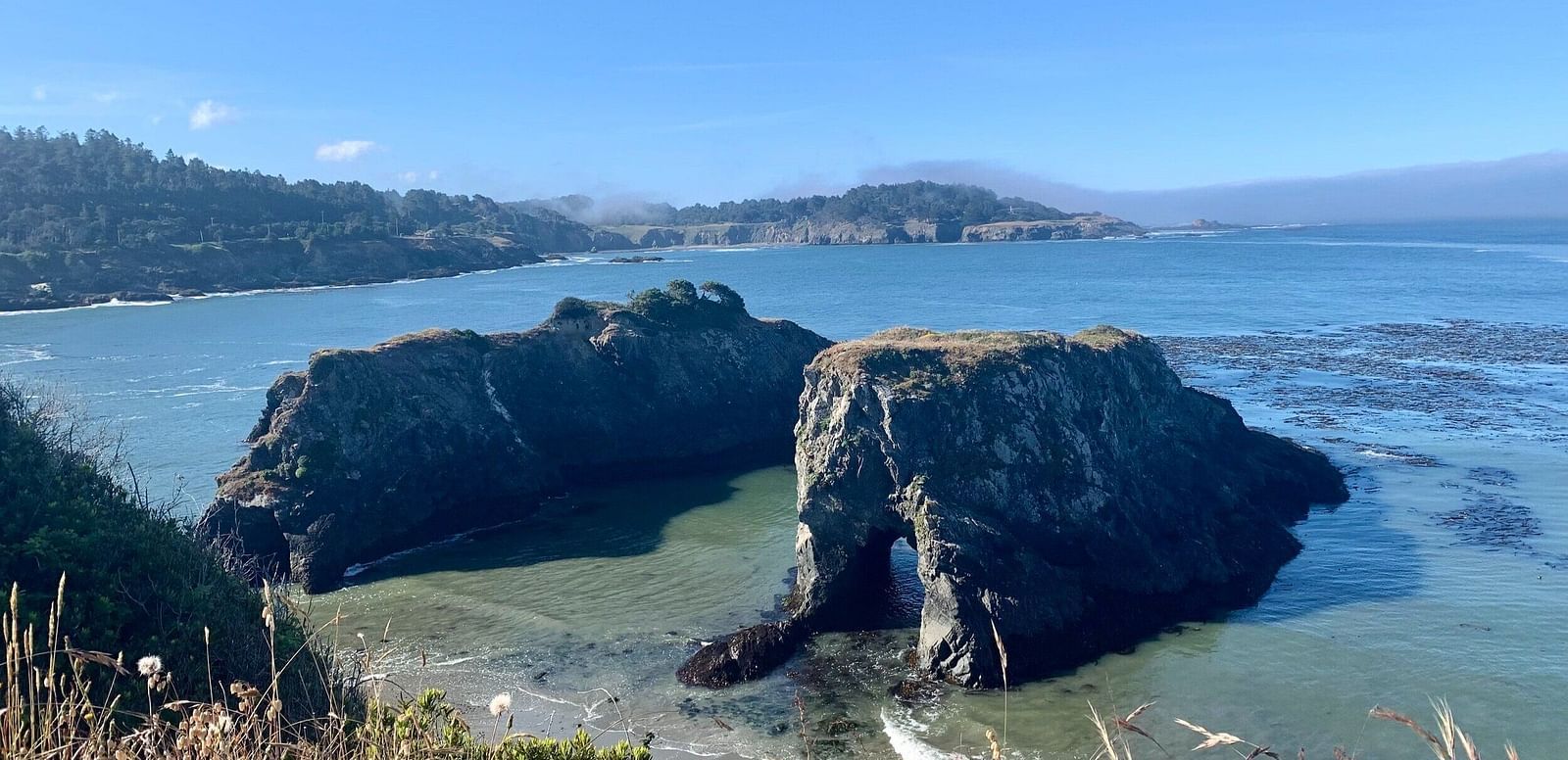 A view from the top of a hill with a vast ocean and two rocky islands in the middle