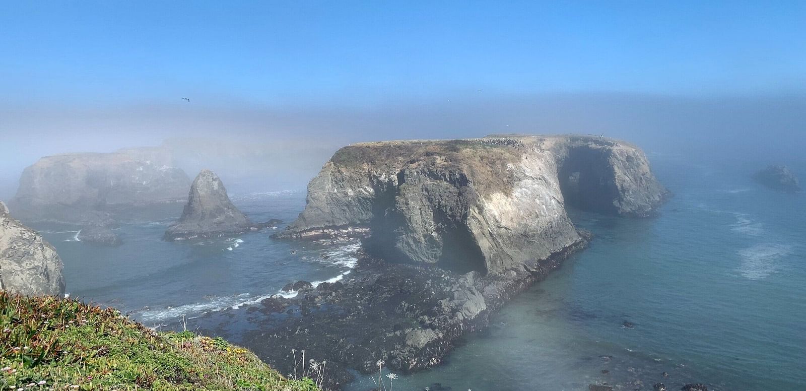A mountain arch with the a number of small rocky structures in the middle of the ocean
