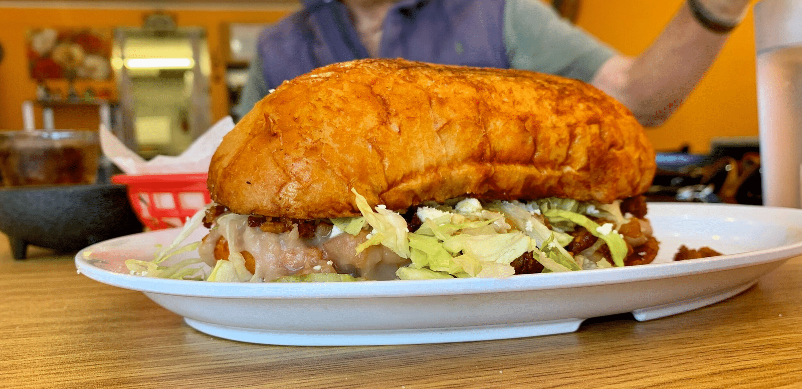 A big burger on a plate with a man in the back