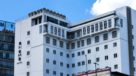 A low-angle exterior view of a tall, white modern building with square windows under a blue and white sky.