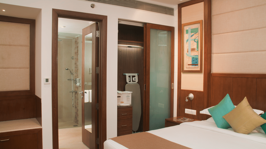 Modern hotel bedroom with glass bathroom, wooden interiors, and cosy bedding at Savoy Suites, Greater Noida