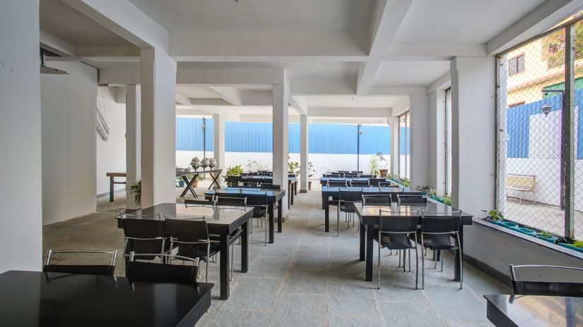Seating arrangement inside the restaurant of Magnus Aerith Studio, Kharadi featuring several sets of tables and chairs and a view of outside world through transparent walls.
