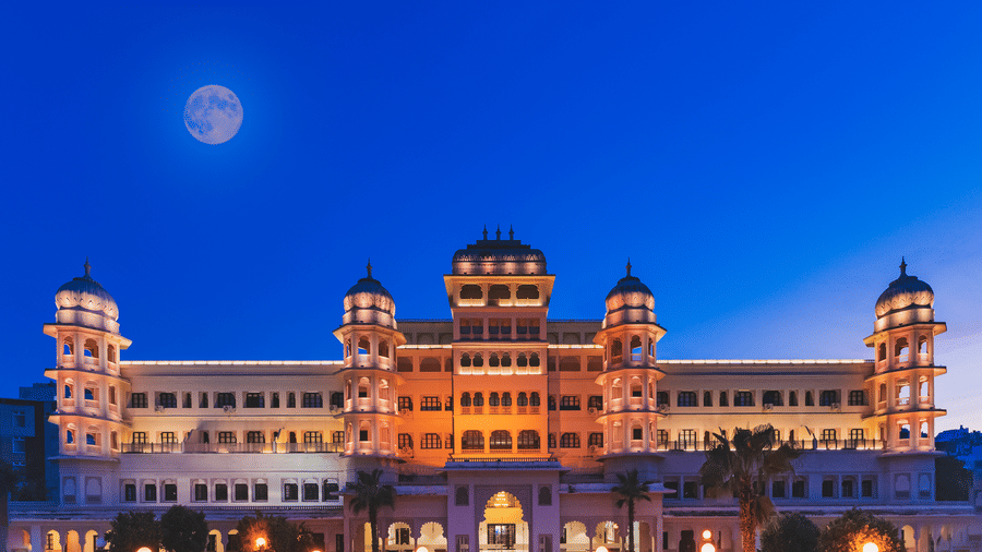 A mesmerising view of the best hotel in Nathdwara, Shri Vallabh Vilas Lords Plaza's facade at night under a twilight sky with a visible moon, featuring domes, towers, and illuminated windows.
