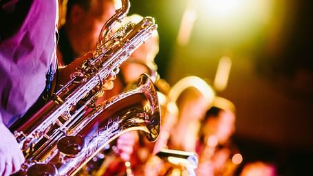 many musicians on the stage playing trumpets with a stage light in the background