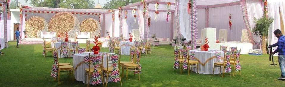 A wedding reception set up on a green lawn with a decorated marquee and chairs for guests at Aamaghati Wildlife Resort.