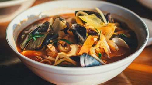 A bowl of stew with different vegetables, fishes and clams. 