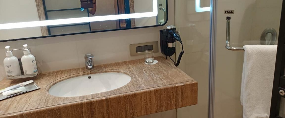 A well-lit bathroom in an executive room at Mirage Hotel, featuring the sink area and a glass partition separating the shower space.