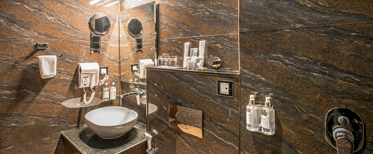 A wide angle shot of the bathroom at Regenta Inn DLS showcasing a wash basin and a commode besides it.