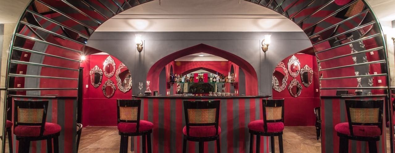 A bar area at Royal Heritage Haveli featuring red walls, arched architectural details, and bar stools.