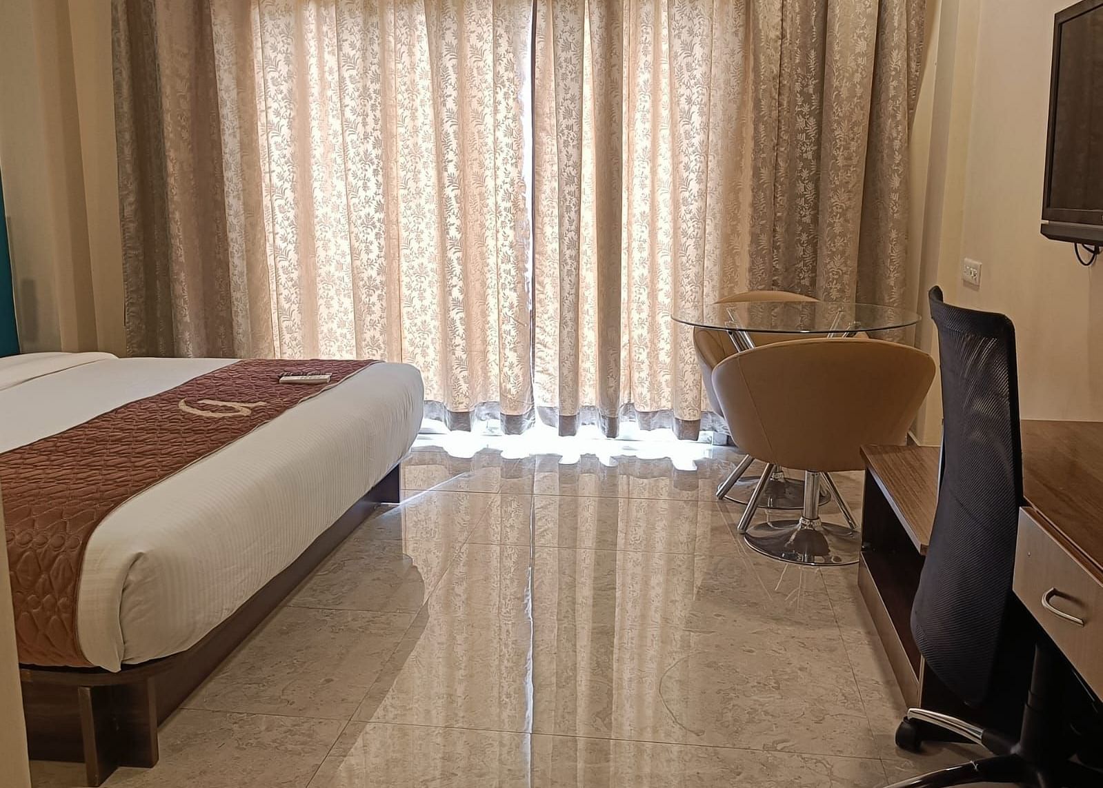 Hotel room interior with a bed, desk, chair, and closed curtains.