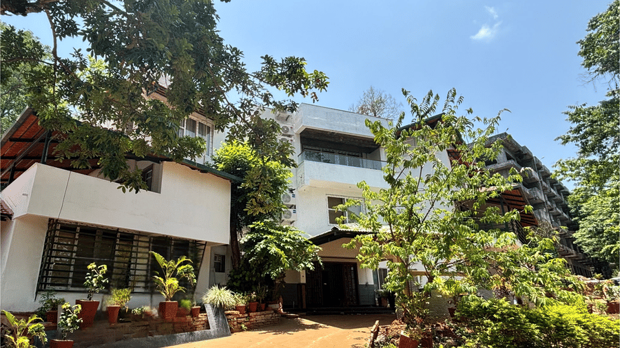 The main building of Lords Riverside Resort, Muduba - Shivamogga surrounded by lush trees and garden plants.