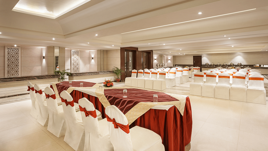 A neatly arranged event space with white covered chairs and burgundy accents prepared for a social event - The Manor, Bareilly