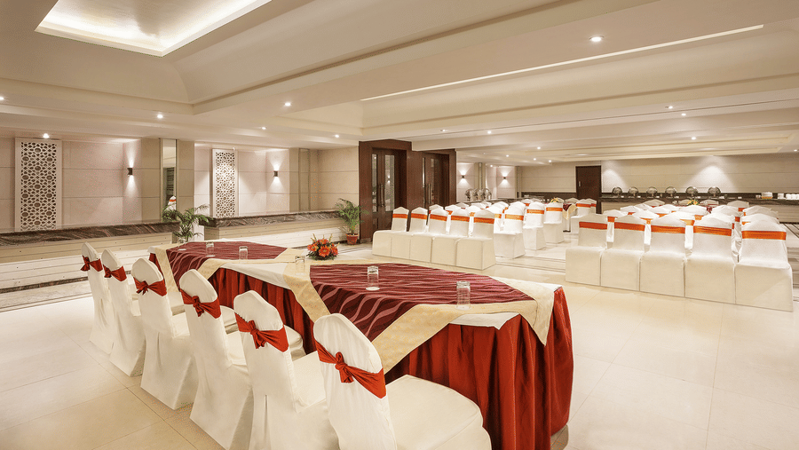 A neatly arranged event space with white covered chairs and burgundy accents prepared for a social event - The Manor, Bareilly