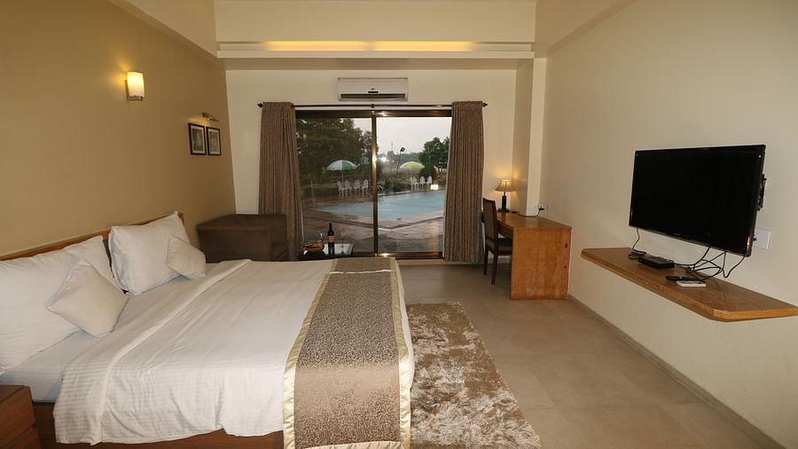 a double bed with side tables and a a floor to ceiling glass door at super deluxe room - VITS Kamats Resort, Silvassa