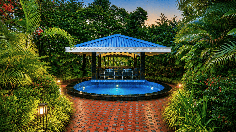 Garden gazebo with a blue pitched roof and a round plunge pool lit at dusk, framed by tropical planting at MAYFAIR Oasis Resort & Convention, Jharsuguda.