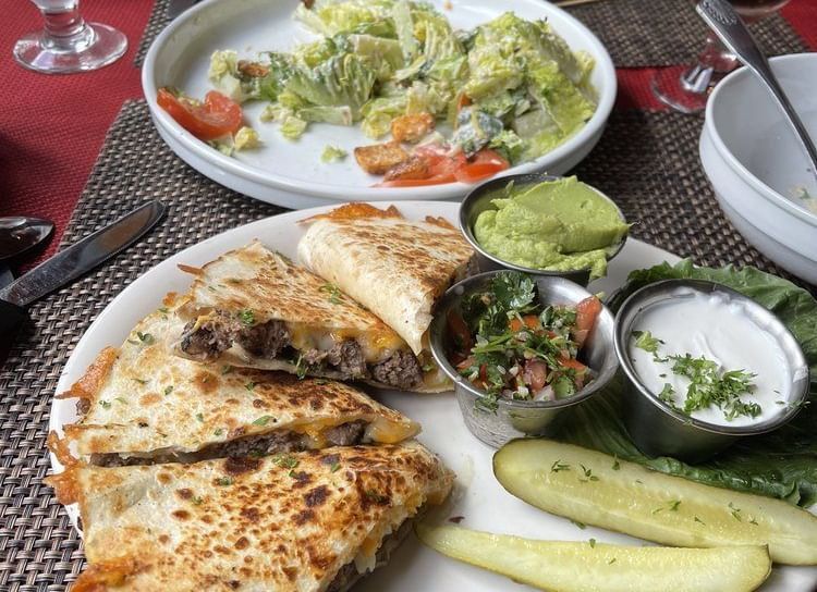 A table setting featuring a meal with a quesadilla, guacamole, salsa, and a side salad