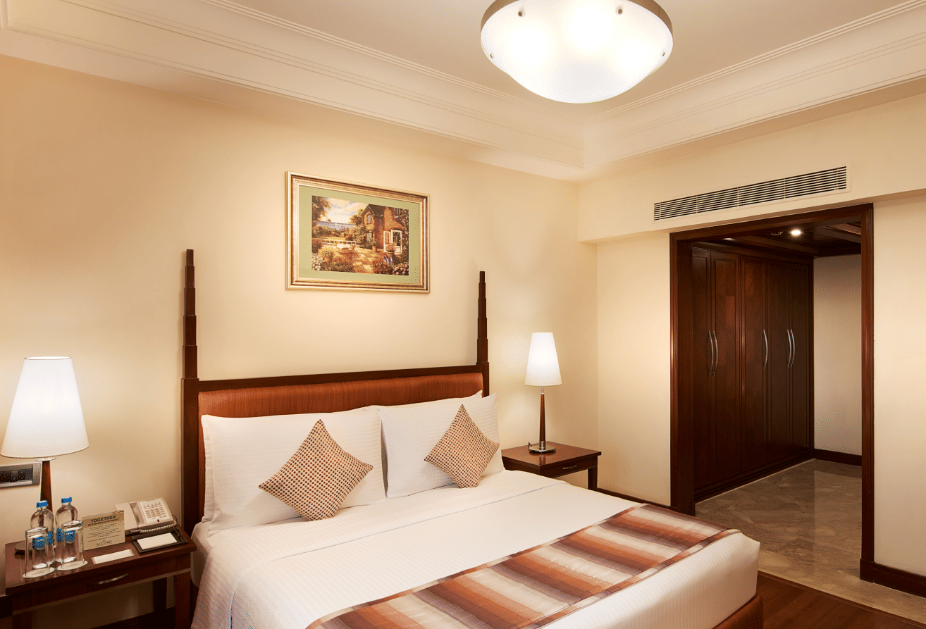 An image of a bedroom featuring a double size bed, bedside table with lamp on either side, and a ceiling light - Accord Metropolitcan