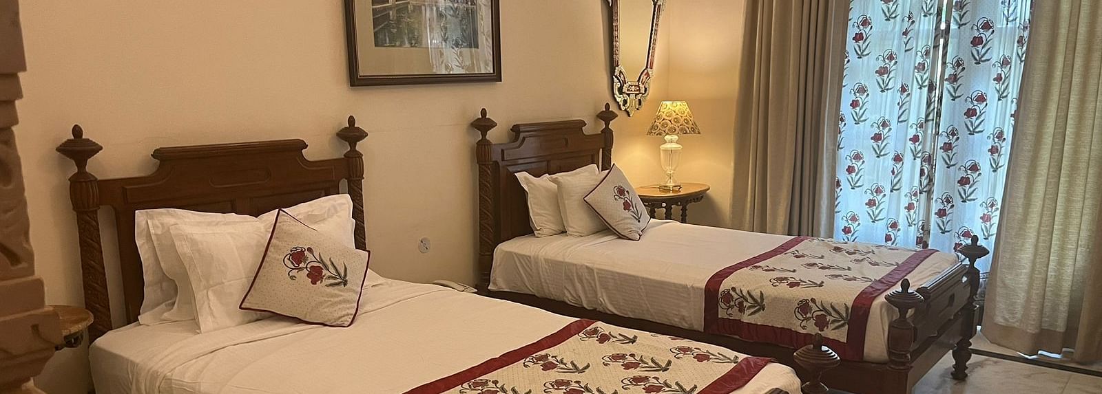 A cosy twin bedroom with carved wooden decor, warm lighting, and traditional accents - Khas Bagh, Jaipur.