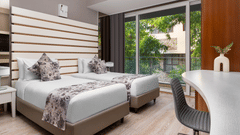  Contemporary room at The Atara, Gurugram featuring two single beds, a white desk, and a balcony view. The room has light wood floors and horizontal wall decor