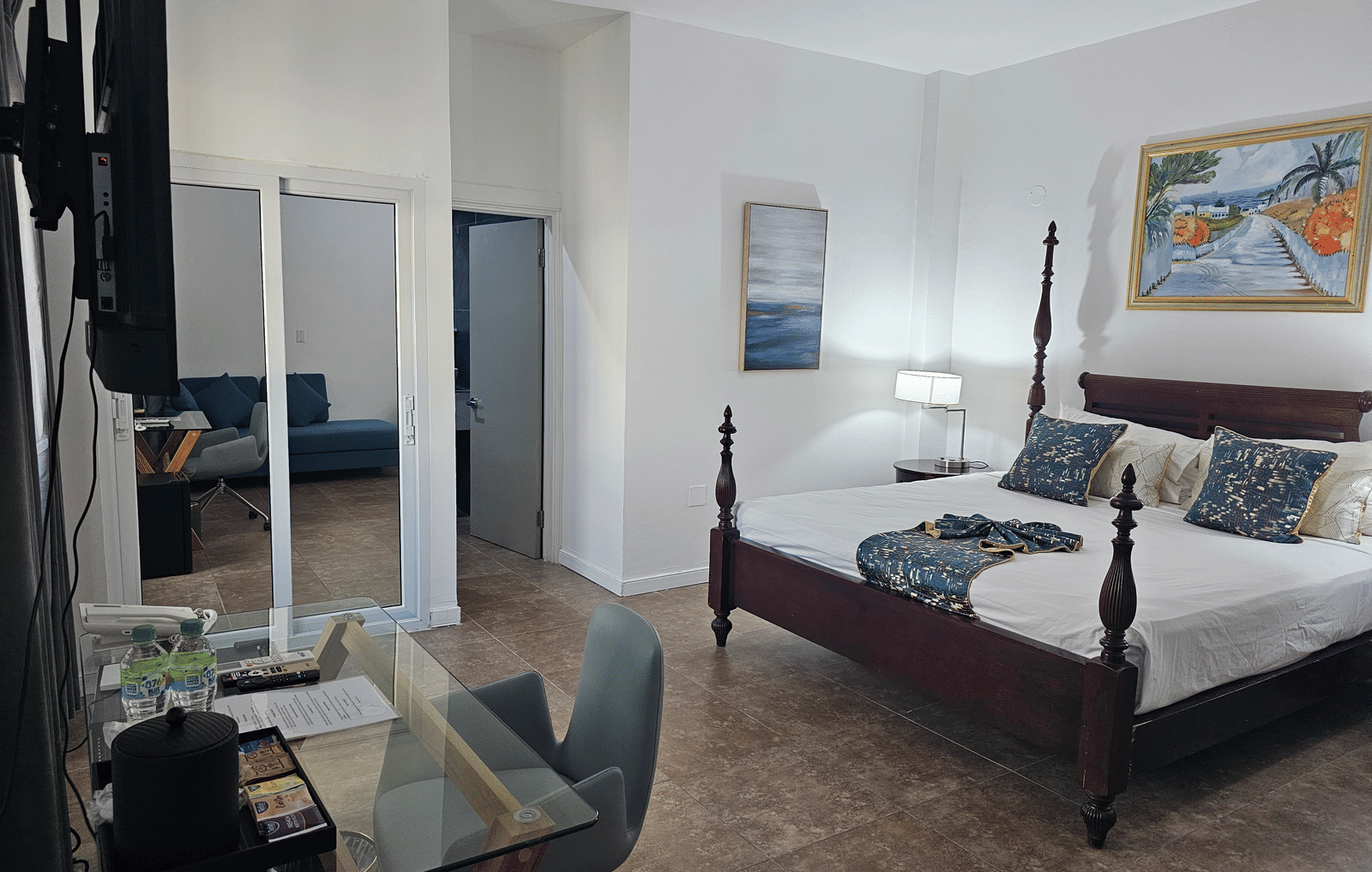 The Junior King Suite at Hotel 39, Jamaica, with a 4-poster bed, a glass-top work desk, a wardrobe, and an open bathroom doorway.