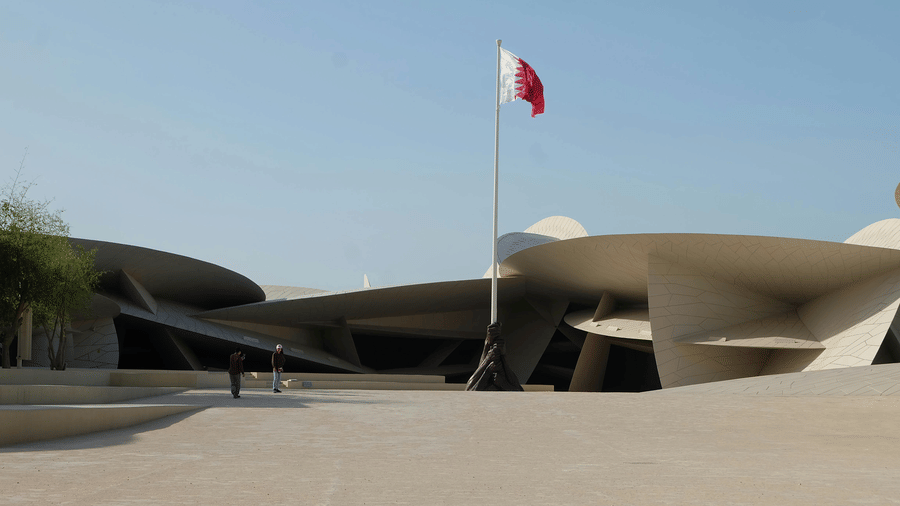 The National Museum of Qatar featuring its iconic interlocking disc architecture and the Qatari flag on a tall pole.