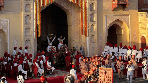 One of the cultural events in Jaipur featuring an armed procession leaving the main arched gates of a fort decorated with flowers.