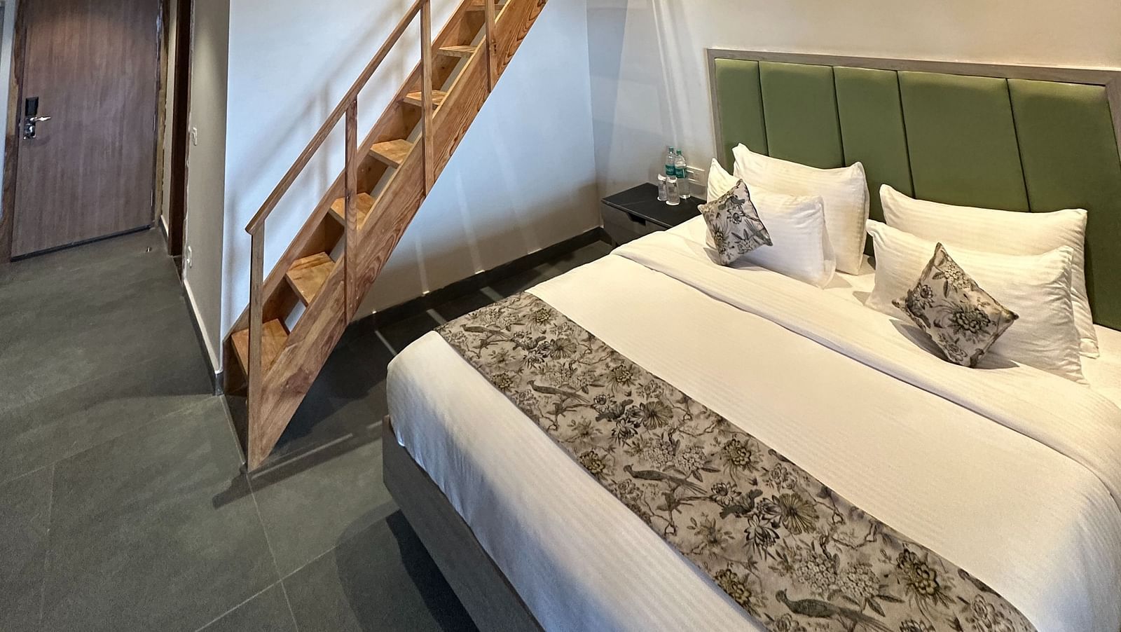 A spacious hotel room with a king-size bed, a wooden ceiling, and a loft area accessible by a staircase.