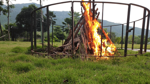 A large bonfire set up in a grassy area surrounded by protective fencing, ready for an evening gathering - Black Thunder, Coimbatore