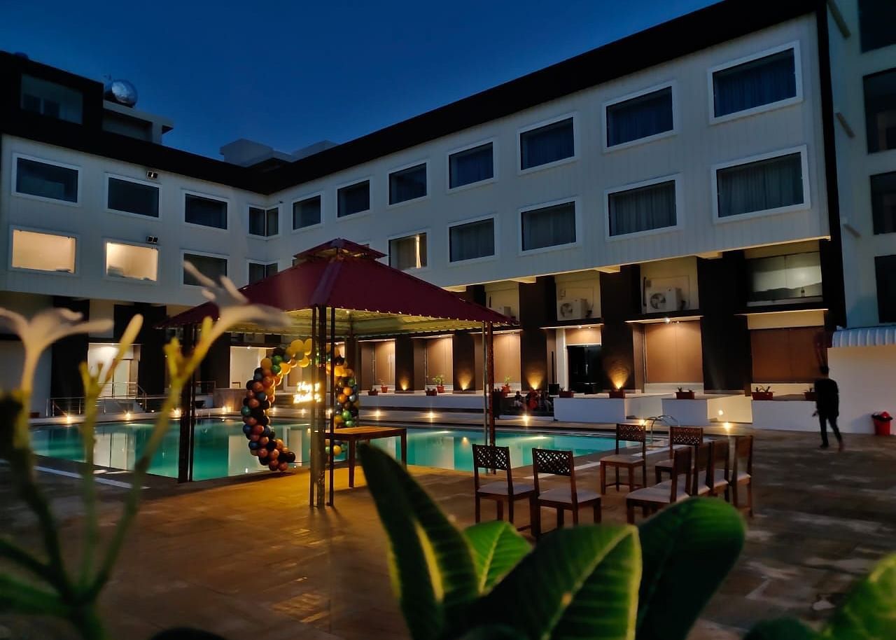 An evening view of a resort building with illuminated windows surrounding a swimming pool - Bamboo Saa Mulberry Resort, Pushkar
