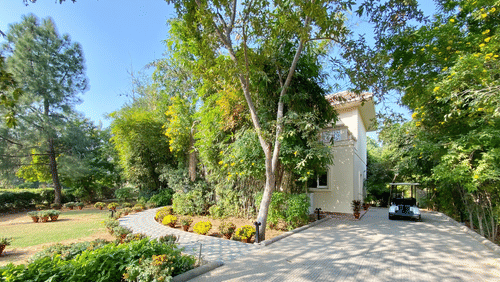 A huge house with green trees and lawn inside the compound, pictured with a golf cart parked on the front of the house - Karma Lakelands.
