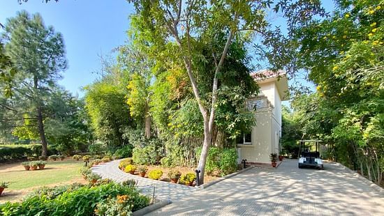 An image showing a huge house with green trees and lawn inside the compound, pictured with a golf cart parked on the front of the house