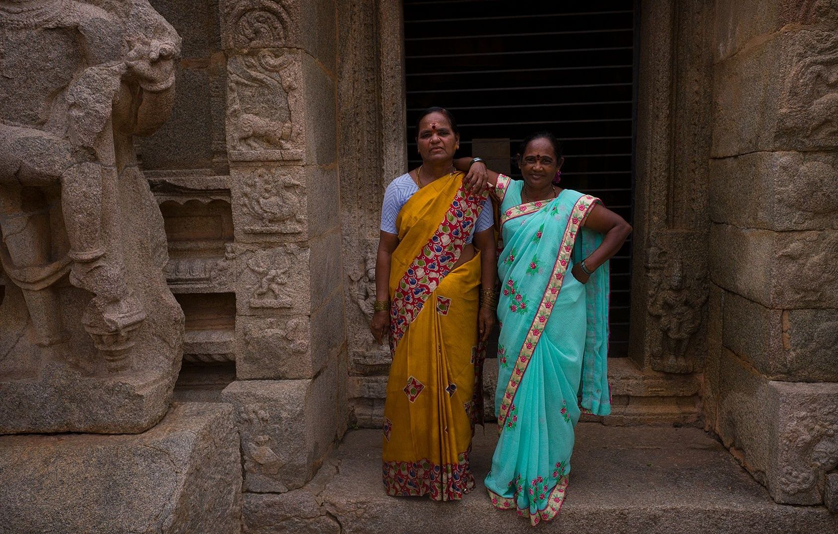 Two women standing by hampi stone temple entrance