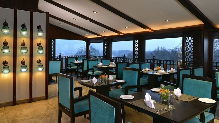 Restaurant at Golden Tulip, Srinagar featuring oragnised tables under ambient lighting with a picturesque view in the background