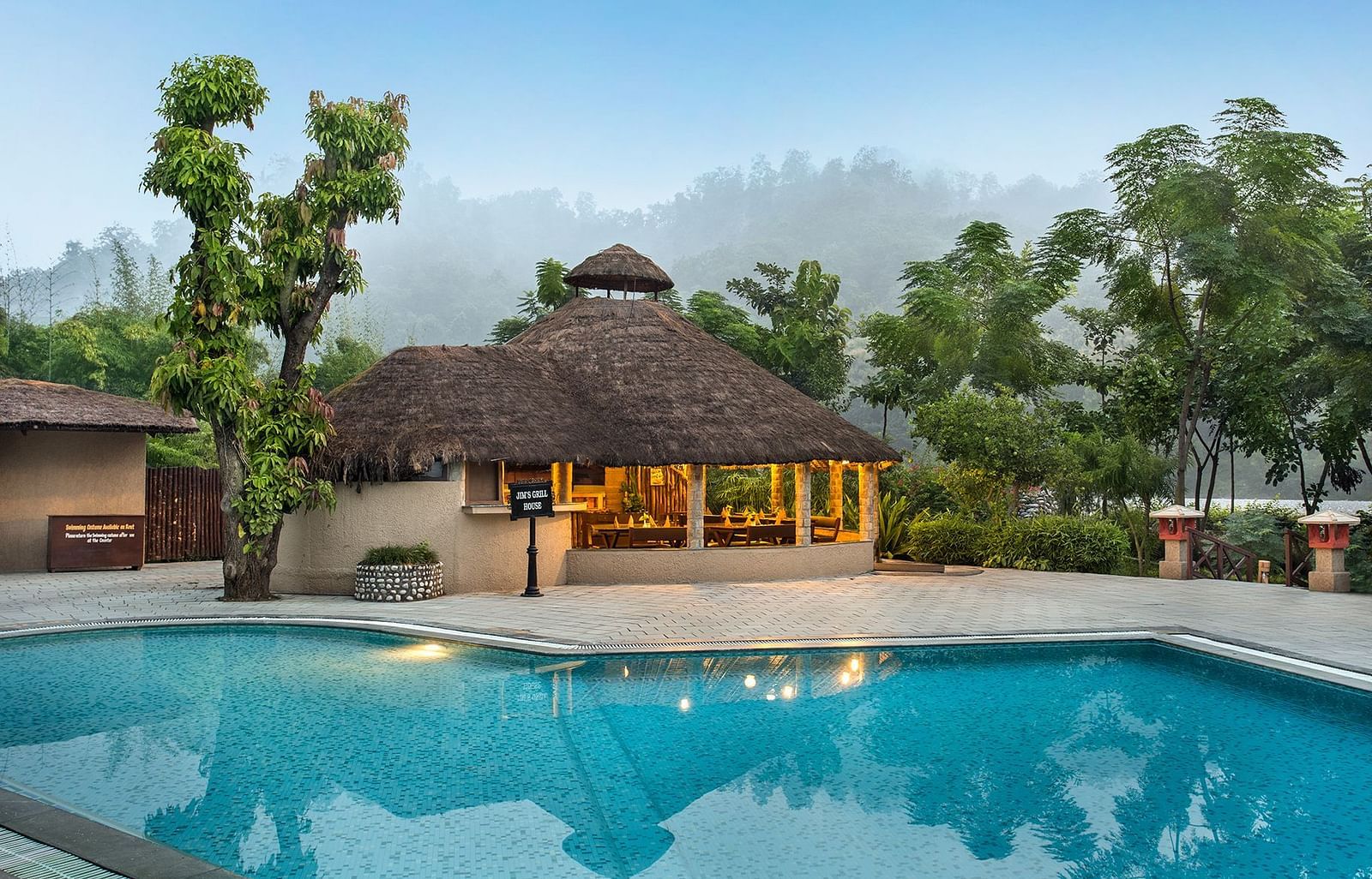 Front view of outdoor swimming pool with a hut, surrounded by lush greenery.