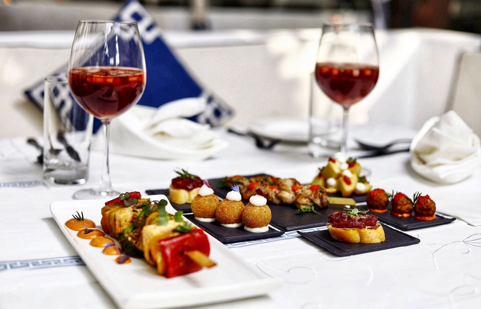 image of a platter of indian starters served with two glasses of wine on a table - The Claridges New Delhi