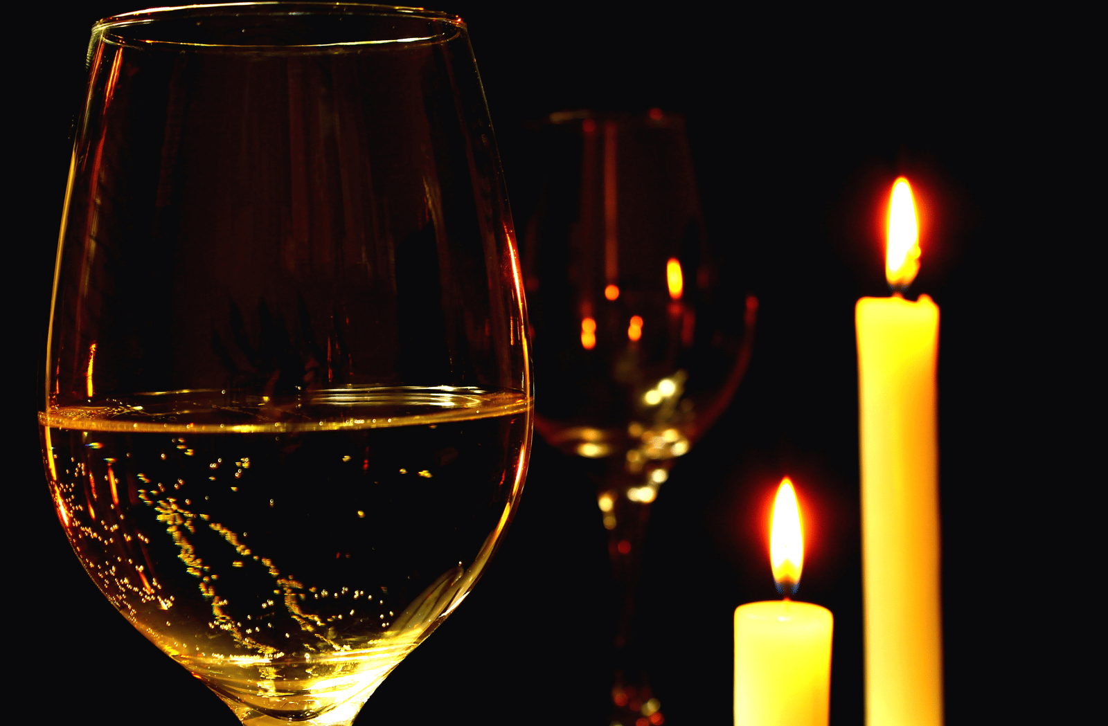 A close up shot of a wine glass with two lit candles next to the glass.